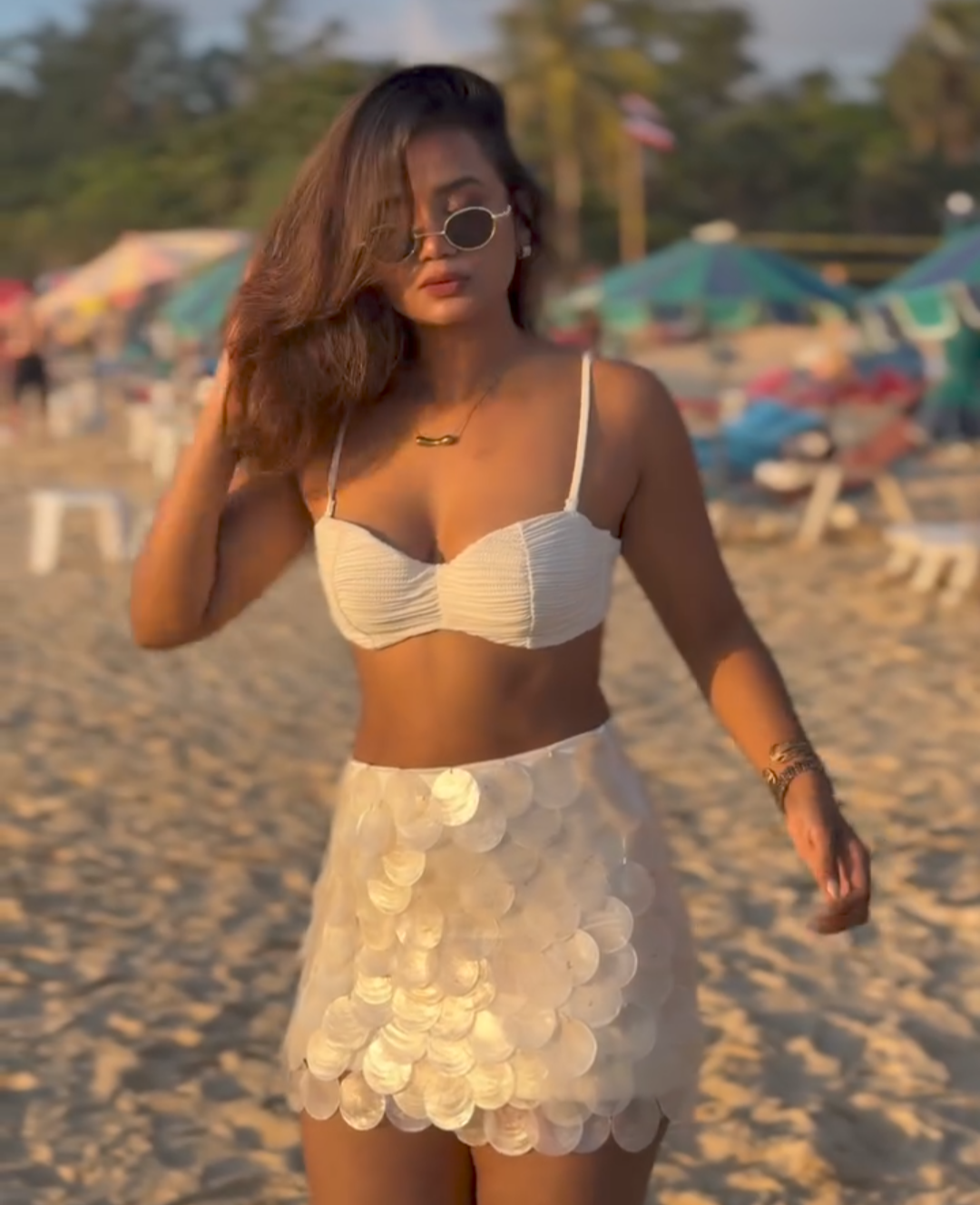 Woman in a white bikini top and skirt on a beach with colorful umbrellas in the background