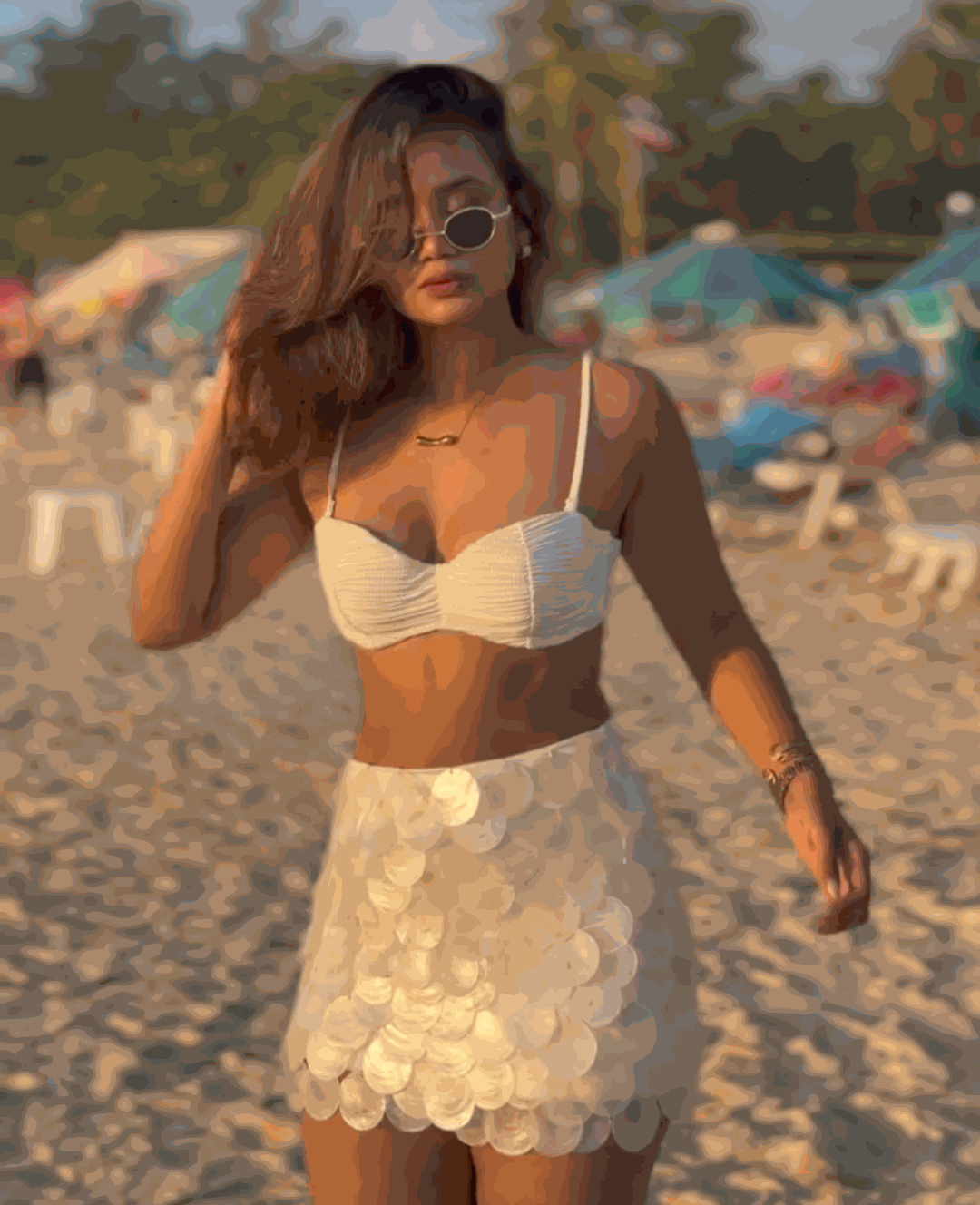 Woman in a white bikini top and skirt on a beach with colorful umbrellas in the background